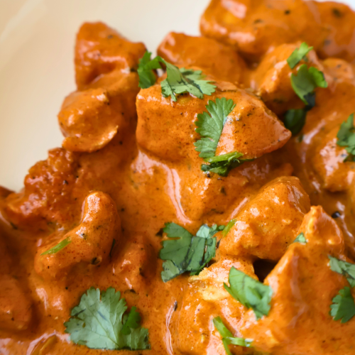 Creamy butter chicken served in a white bowl, featuring tender chicken pieces coated in a rich tomato and butter curry sauce, garnished with fresh cilantro.