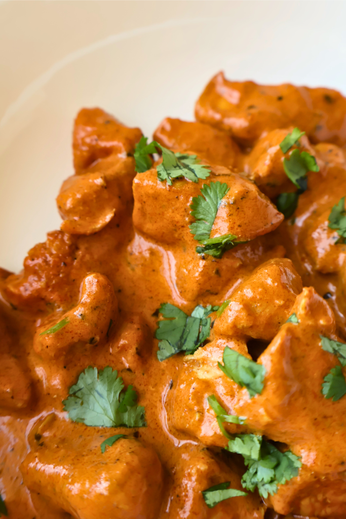 Creamy butter chicken served in a white bowl, featuring tender chicken pieces coated in a rich tomato and butter curry sauce, garnished with fresh cilantro.