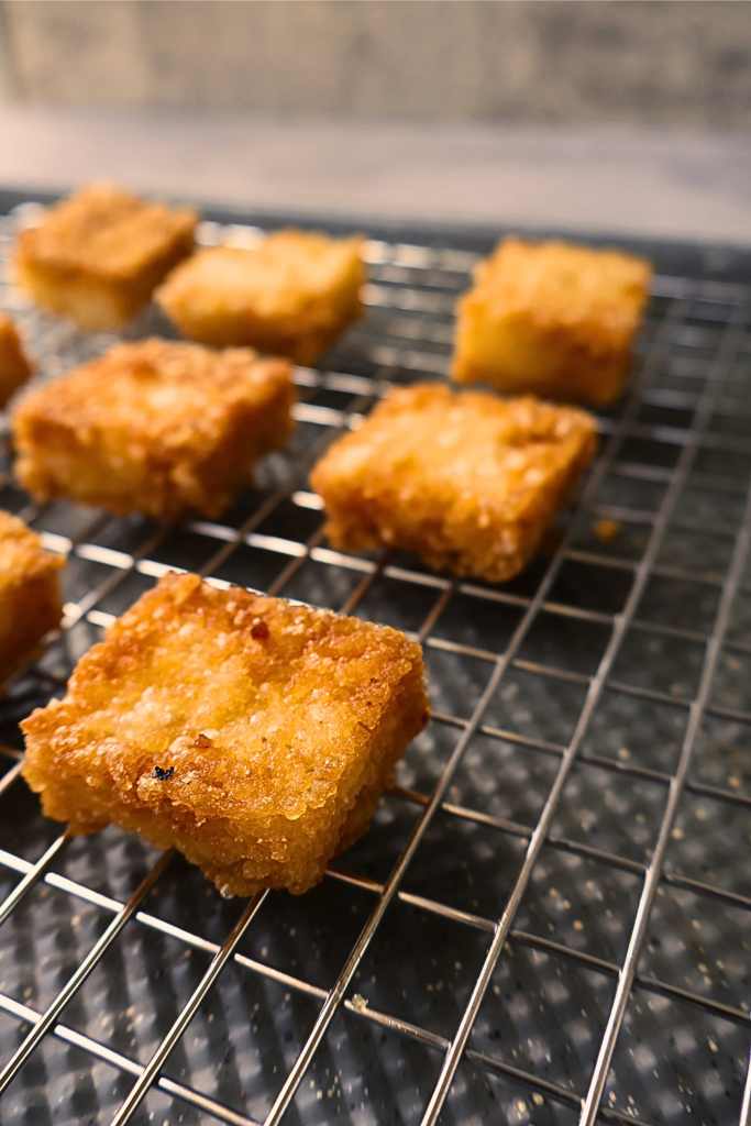 Golden crispy sushi rice squares cooling on a wire rack after frying, ready to be topped with spicy tuna and Japanese mayonnaise.