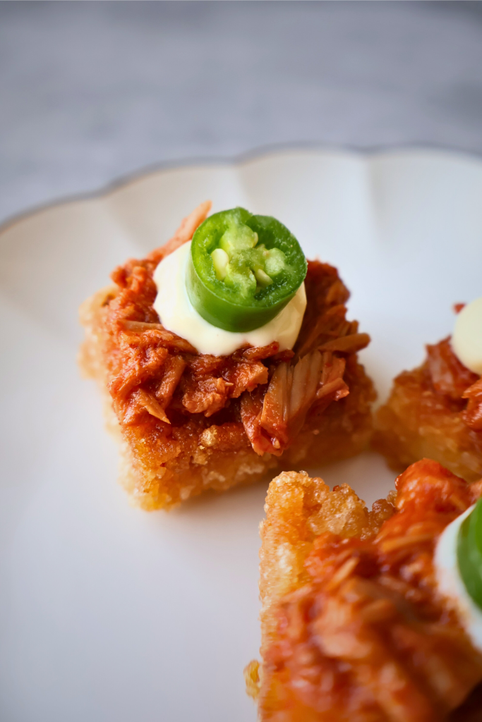 Overhead view of spicy tuna crispy rice topped with sliced jalapeños, arranged on a white plate in a Japanese fine dining presentation.