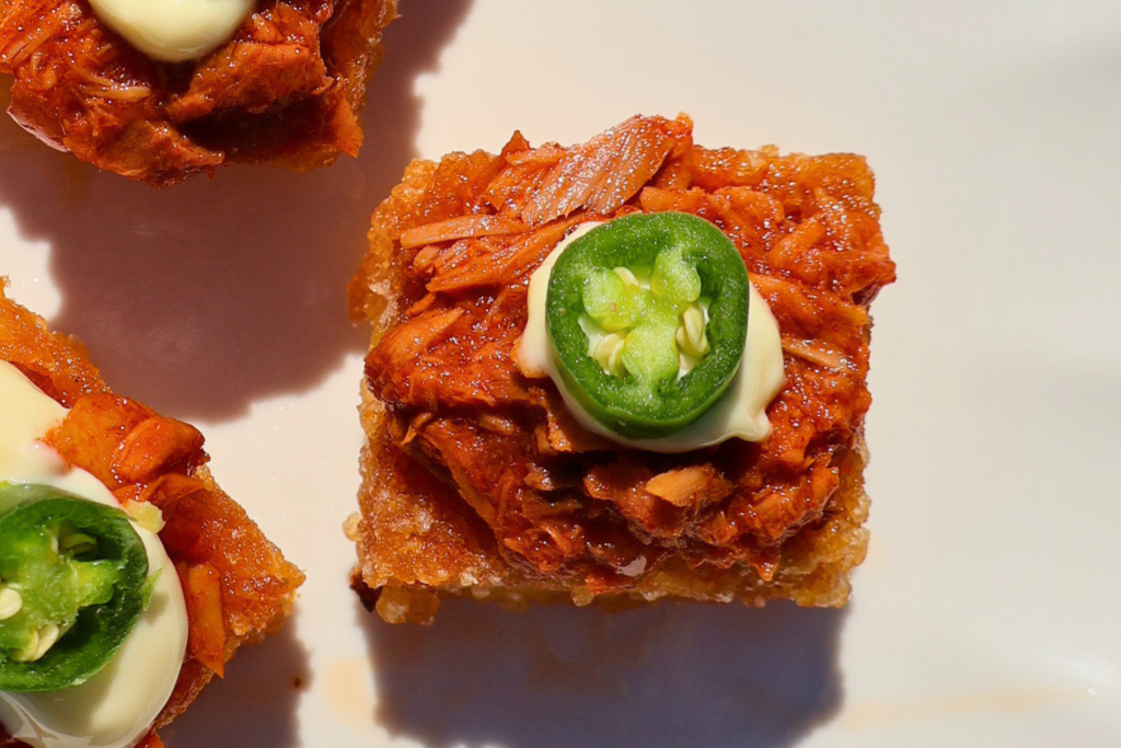 Close-up of crispy sushi rice topped with spicy tuna, Japanese mayonnaise, and fresh jalapeño slices on a white plate.