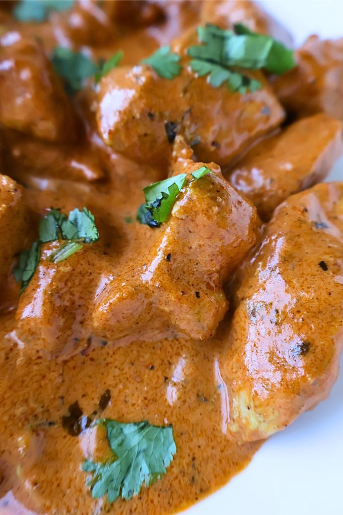 Creamy butter chicken served in a white bowl, featuring tender chicken pieces coated in a rich tomato and butter curry sauce, garnished with fresh cilantro.