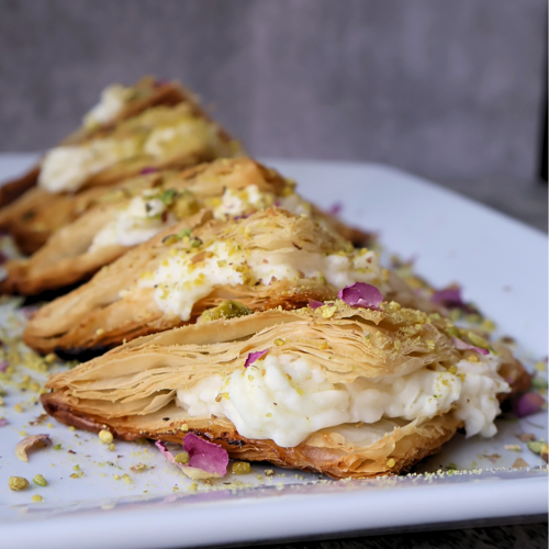 Traditional Middle Eastern warbat pastries filled with creamy ashta, arranged on a serving platter and topped with crushed pistachios and dried rose petals.