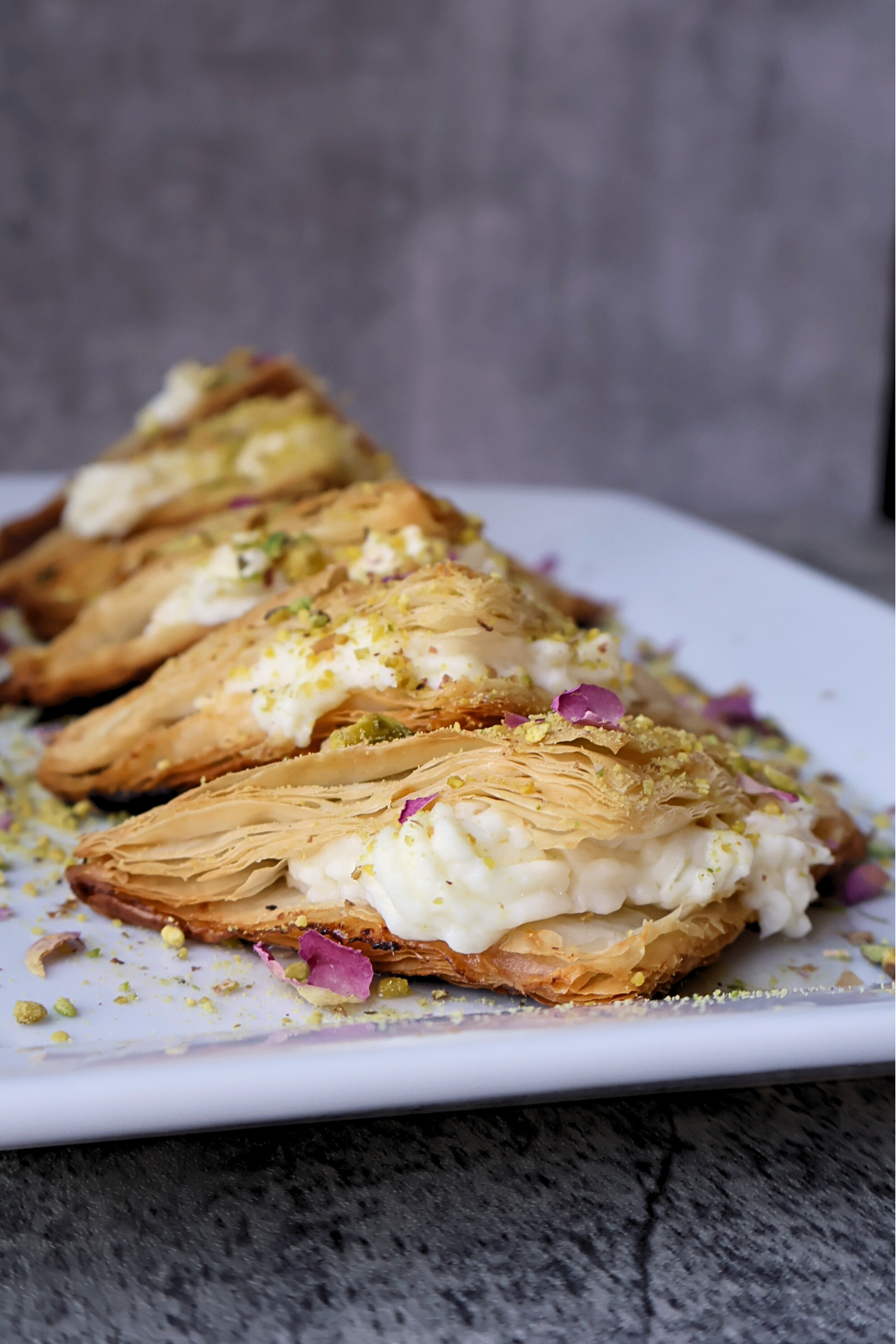 Traditional Middle Eastern warbat pastries filled with creamy ashta, arranged on a serving platter and topped with crushed pistachios and dried rose petals.