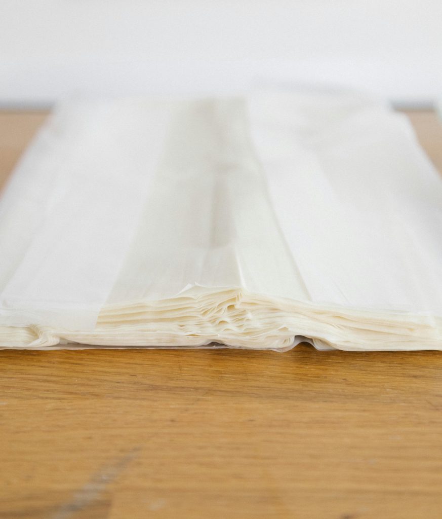 Stack of thin phyllo dough sheets on a wooden surface, ready for making pastries such as baklava, börek, and warbat.