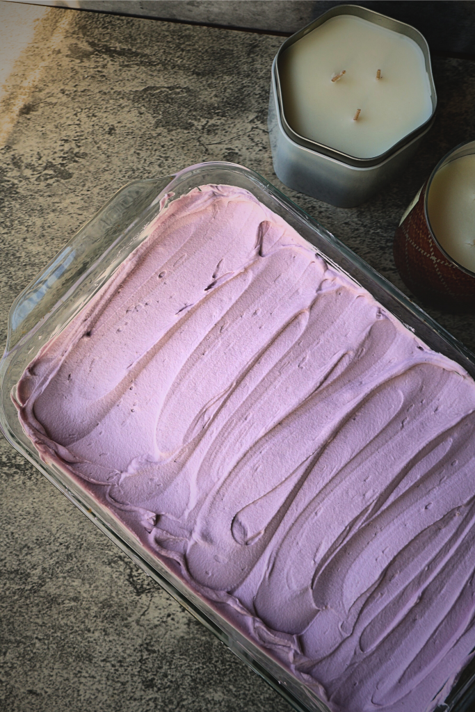 Freshly frosted homemade tres leches cake with smooth purple whipped frosting spread evenly in a baking dish.