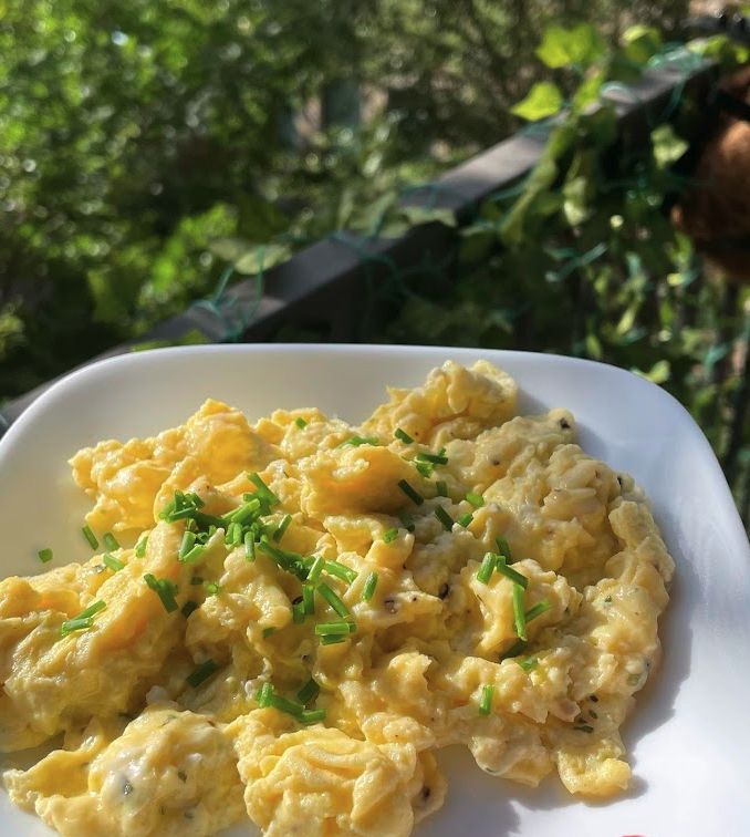 Creamy scrambled eggs made with Boursin cheese, garnished with fresh chives and served on a white plate.