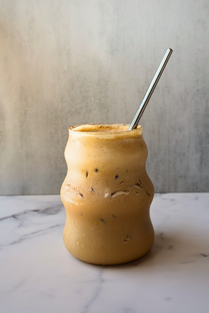 Creamy iced coffee served in a glass jar with ice cubes and a reusable metal straw on a marble countertop.