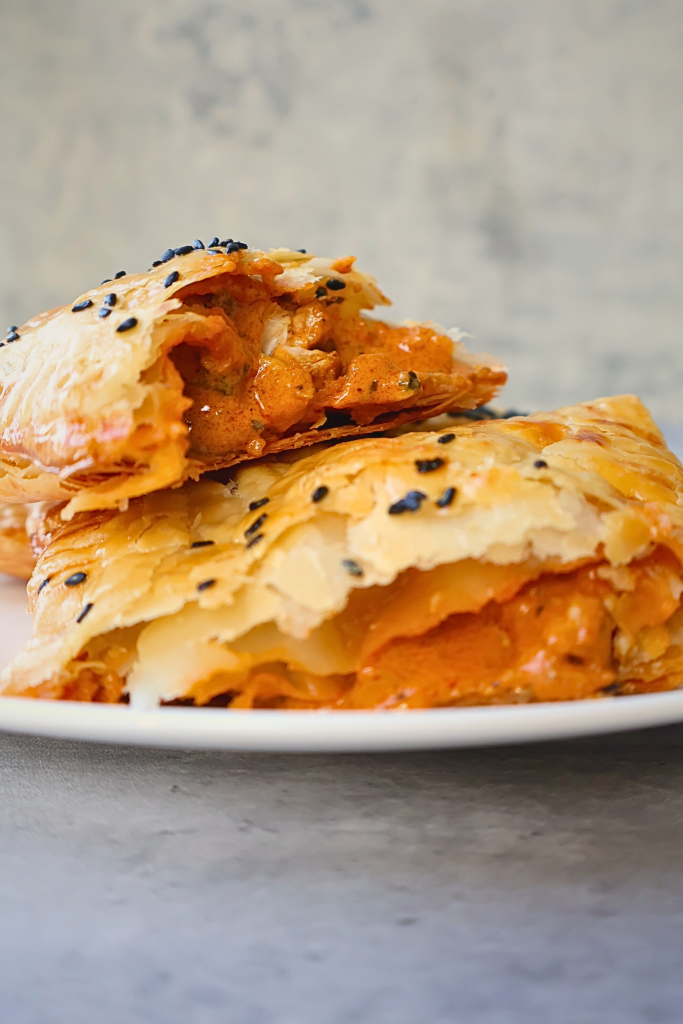 Crispy phyllo pastry pockets filled with creamy butter chicken, baked until golden brown and sprinkled with black sesame seeds.