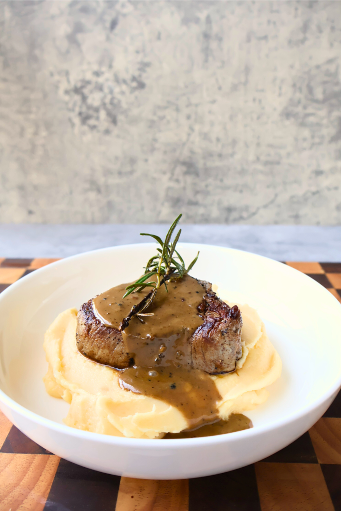 Pan-seared filet mignon served over creamy French aligot with a rich peppercorn sauce and fresh rosemary garnish.