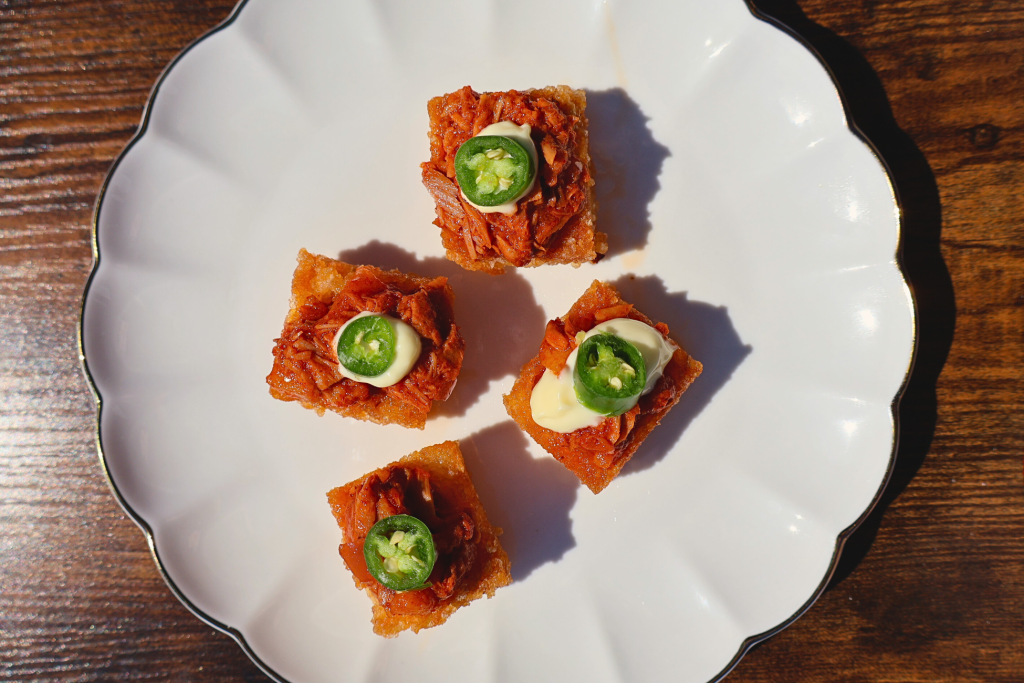 Overhead view of spicy tuna crispy rice topped with sliced jalapeños, arranged on a white plate in a Japanese fine dining presentation.