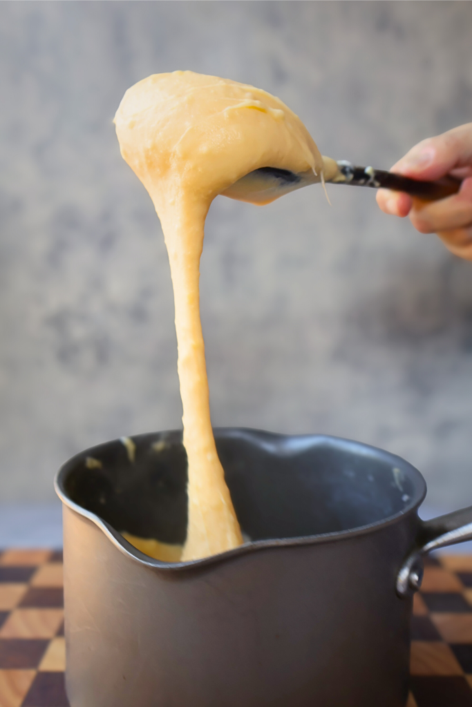 Traditional French aligot being lifted from a saucepan, showcasing its signature long, stretchy texture made from mashed potatoes and melted cheese.