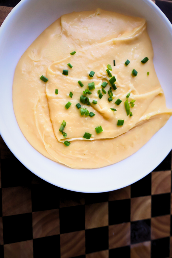 Creamy French aligot made with mashed potatoes and melted cheese, garnished with fresh chives and served in a white bowl.
