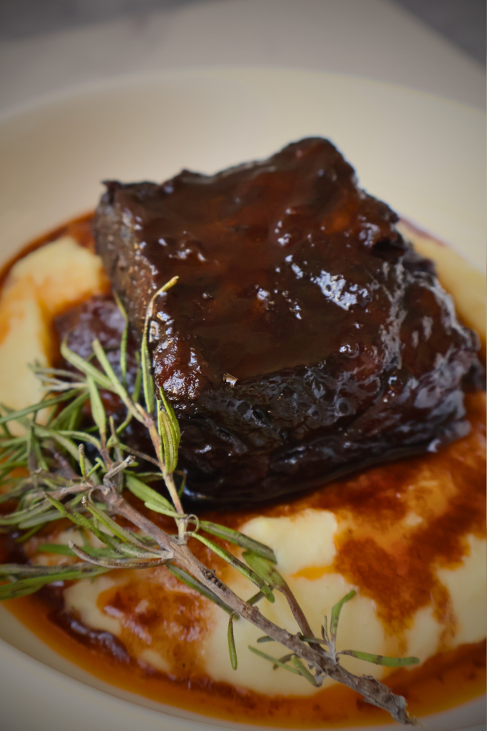 Slow-braised beef short ribs served over creamy mashed potatoes with rich red wine sauce and fresh thyme garnish.