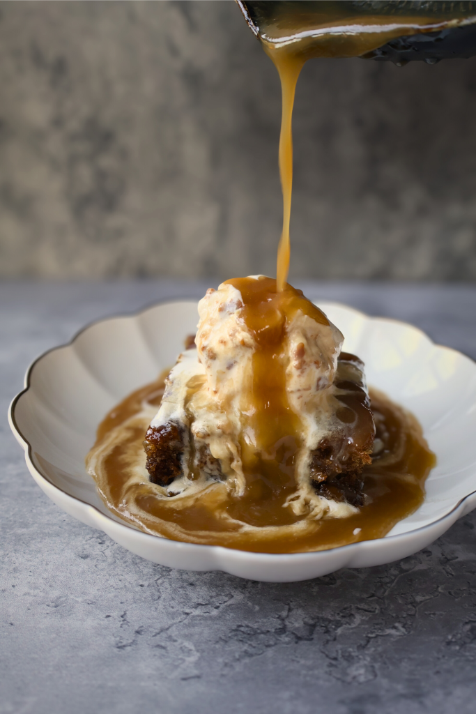 Warm sticky toffee pudding topped with vanilla ice cream as rich homemade toffee sauce is poured over the dessert.