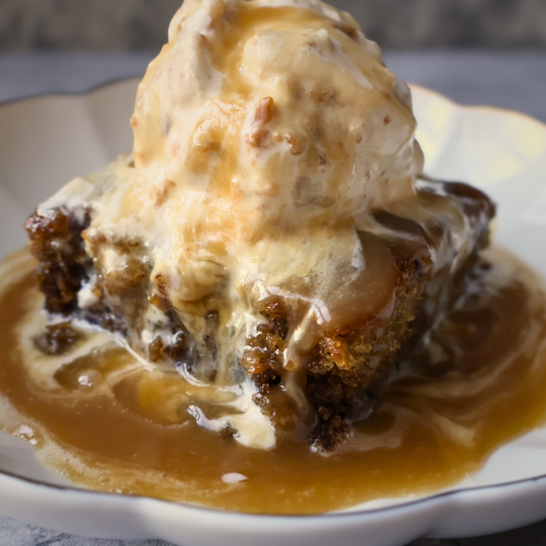 Sticky toffee pudding topped with warm toffee sauce and served with a scoop of vanilla ice cream.