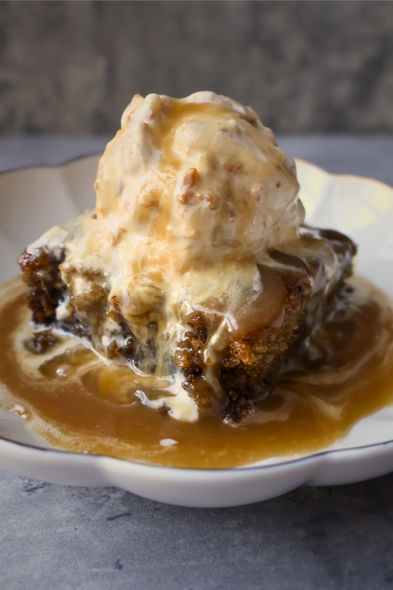 Sticky toffee pudding topped with warm toffee sauce and served with a scoop of vanilla ice cream.