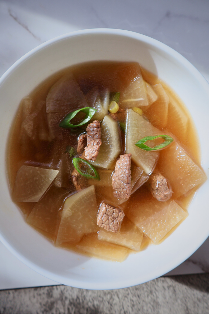 Top view of Korean mu guk with beef, radish slices, and green onions in a clear light broth