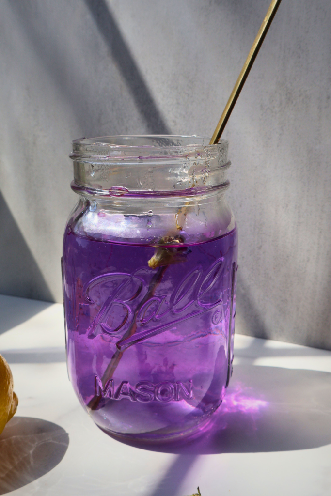 Purple butterfly pea lemon drink in a glass jar with straw on a light background