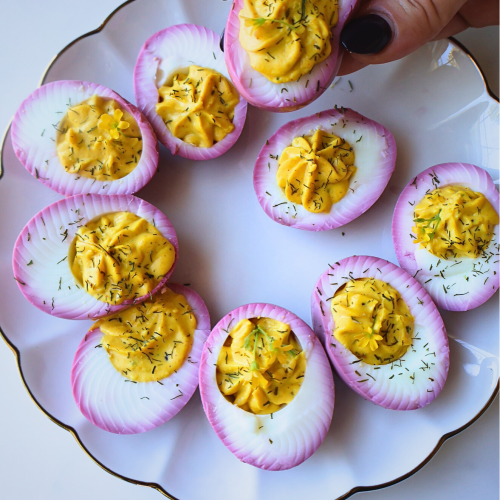 Beet-stained deviled eggs with creamy paprika yolk filling and dill garnish served on a white scalloped plate