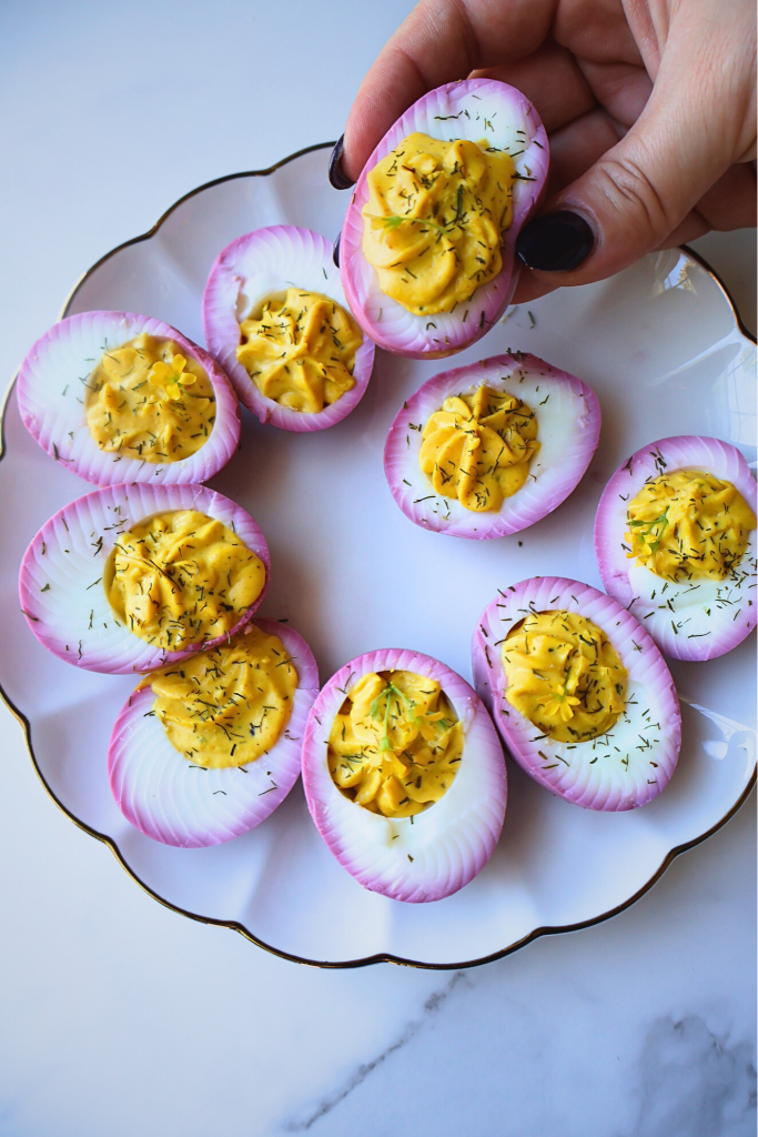 Beet-stained deviled eggs with creamy paprika yolk filling and dill garnish served on a white scalloped plate