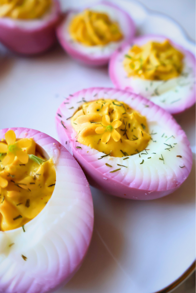 Pink deviled eggs made with beet-colored filling, garnished with fresh dill arranged on a white serving platter.