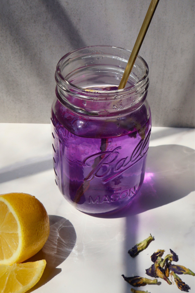Purple butterfly pea drink in a glass jar with lemon slices and dried flowers on a light background