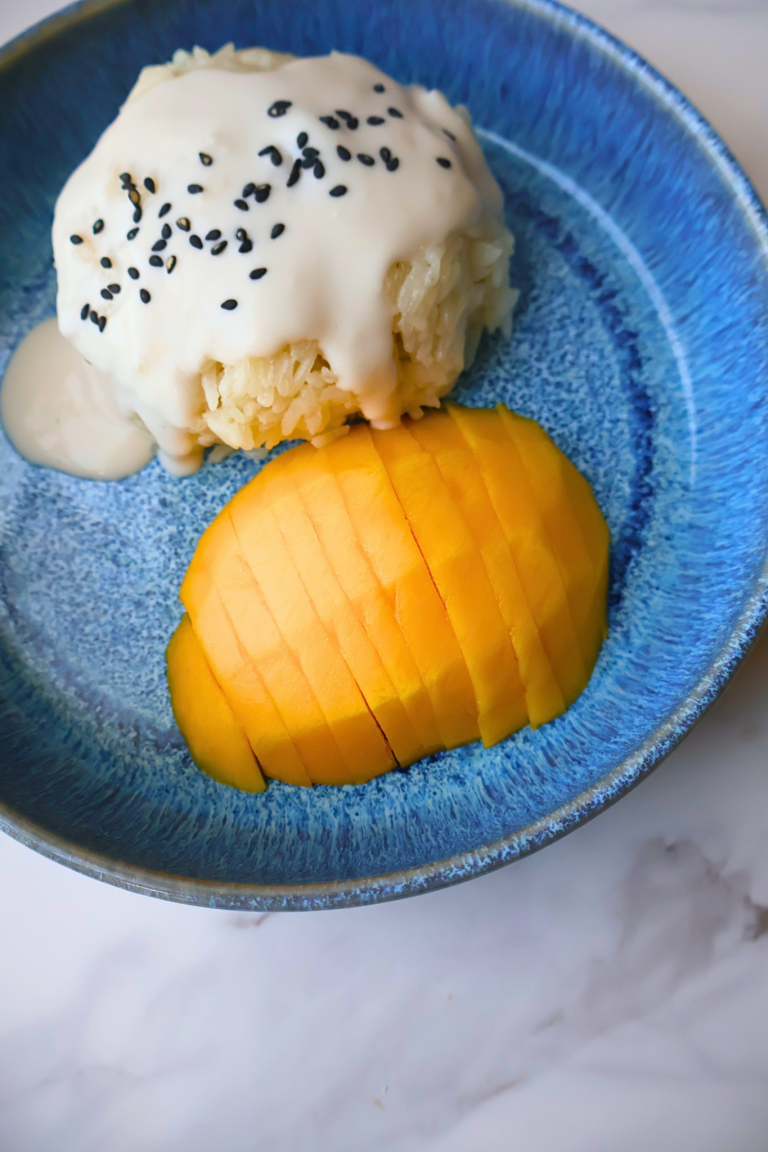 Thai mango sticky rice with coconut cream and black sesame seeds served with sliced ripe mango on blue plate