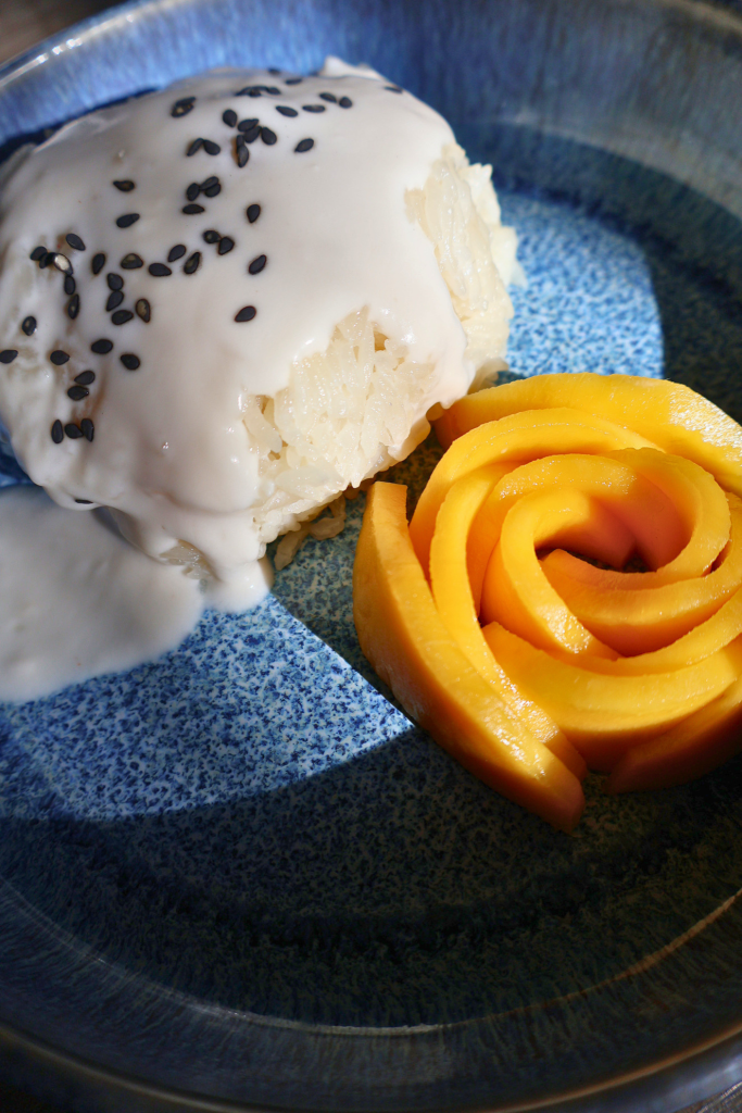 Mango sticky rice with coconut cream and black sesame seeds served with mango rose garnish