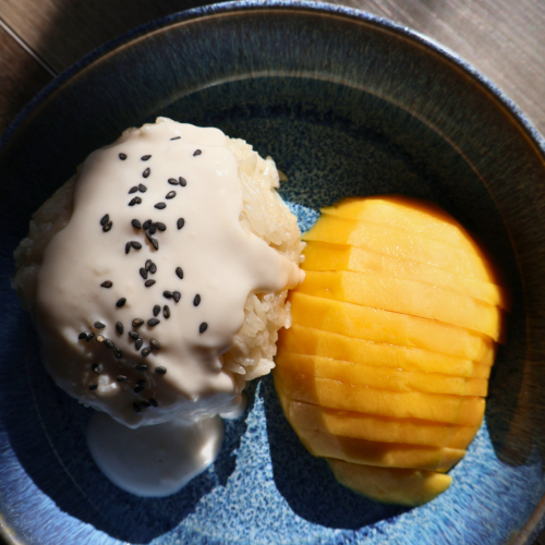 Mango sticky rice with coconut cream and black sesame seeds alongside sliced ripe mango