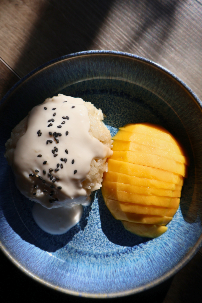 Mango sticky rice with coconut cream and black sesame seeds alongside sliced ripe mango