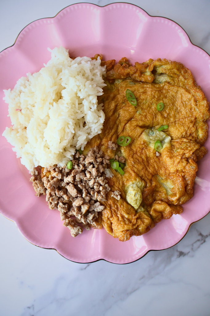 Overhead view of Thai omelet with jasmine rice and minced pork on pink plate