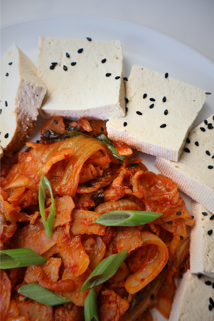 Close-up of dubu kimchi featuring silky tofu topped with spicy sautéed kimchi and garnished with diagonally sliced green onions.