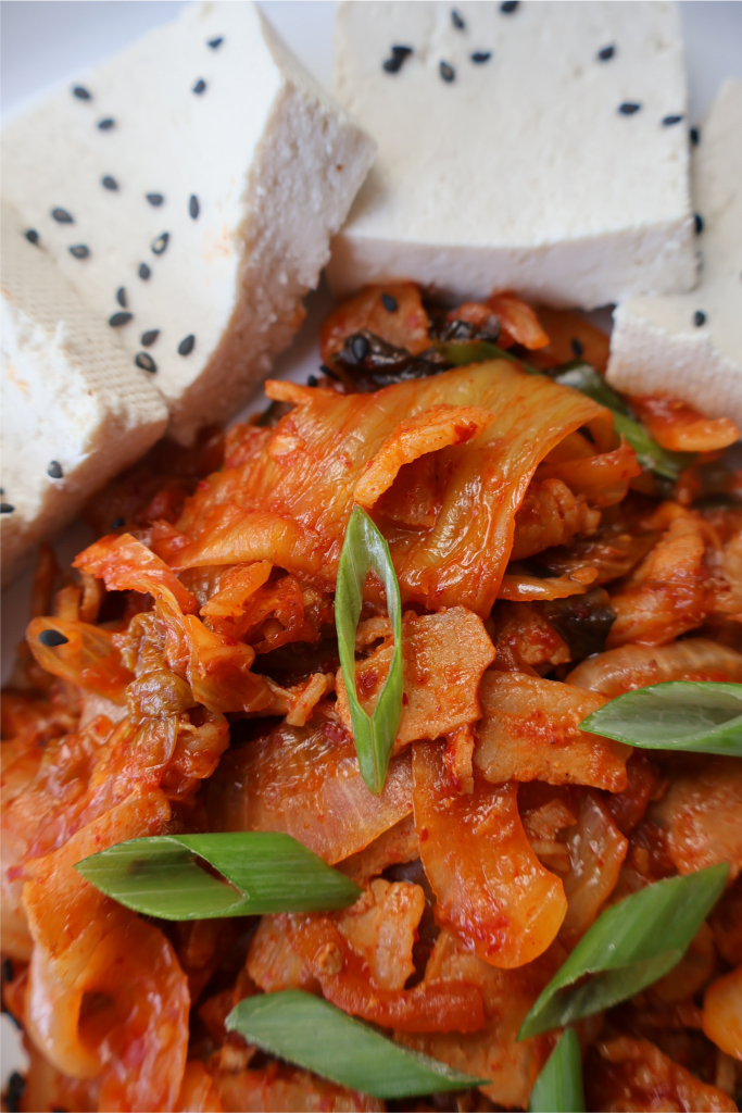 Close-up of dubu kimchi featuring silky tofu topped with spicy sautéed kimchi and garnished with diagonally sliced green onions.