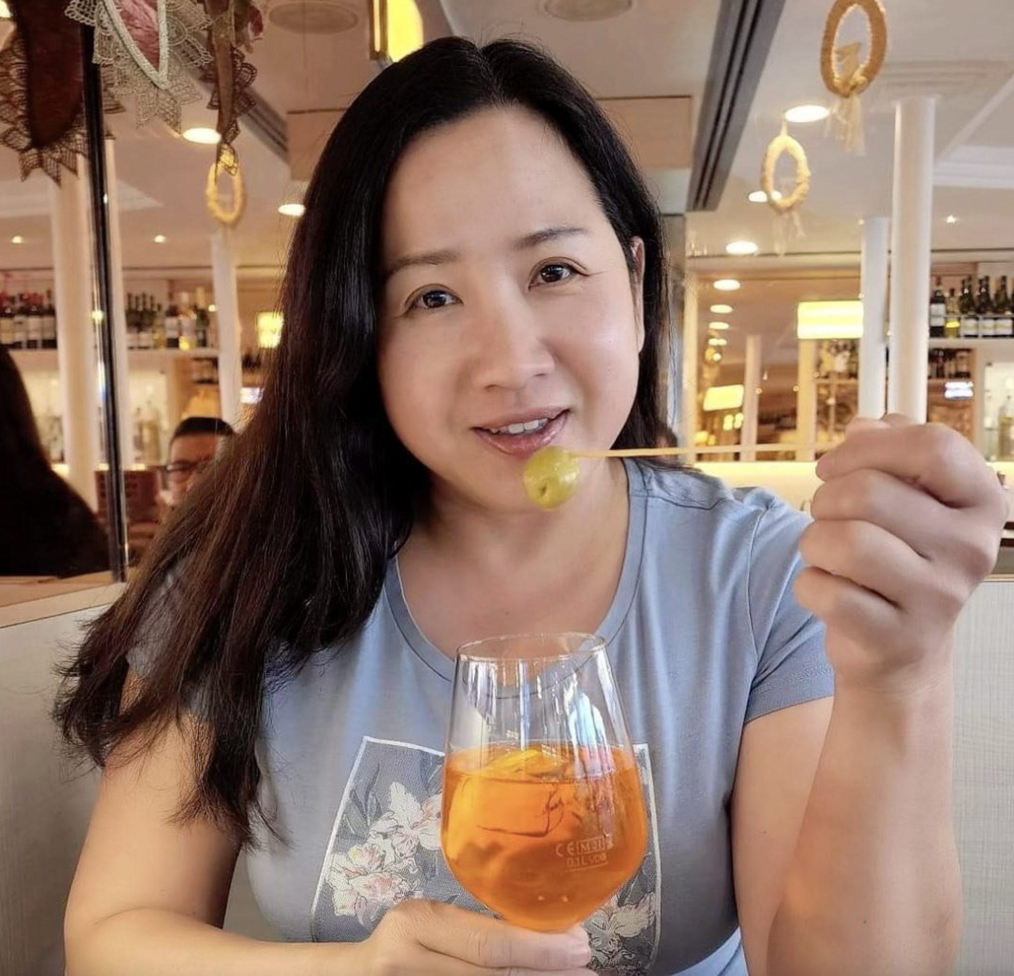 Woman enjoying a drink and tasting food in a restaurant, smiling while holding a fork and cocktail