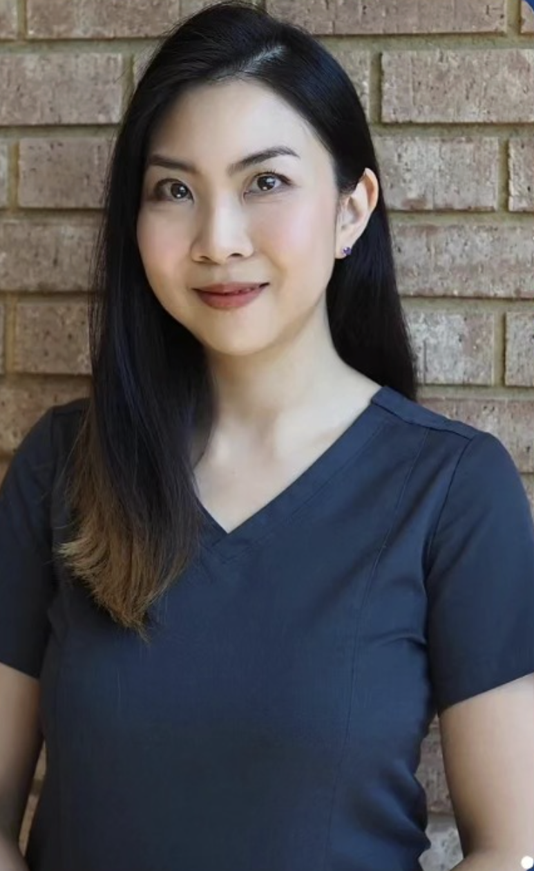Nam portrait smiling in front of a brick wall, wearing a dark top