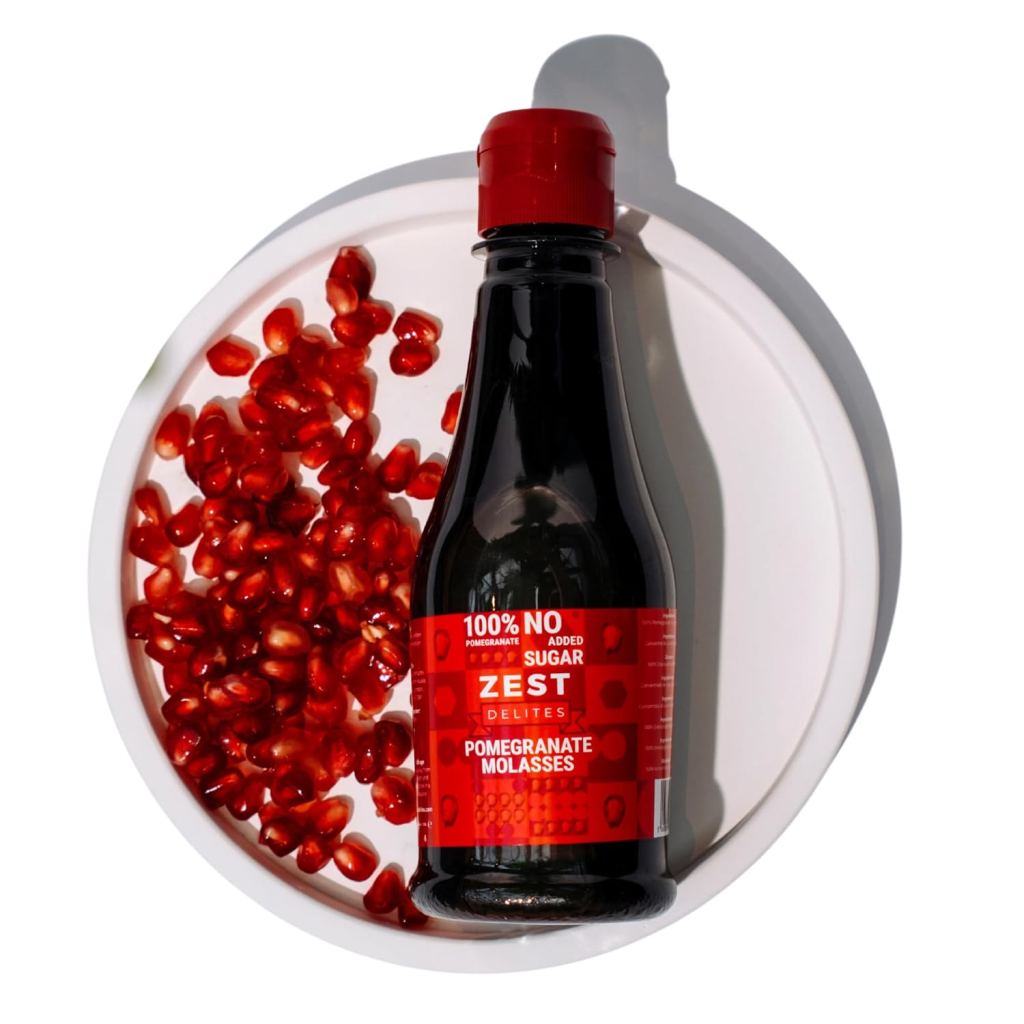 Bottle of Zest pomegranate molasses on a white plate surrounded by fresh pomegranate seeds, the key secret ingredient in this shakshuka recip