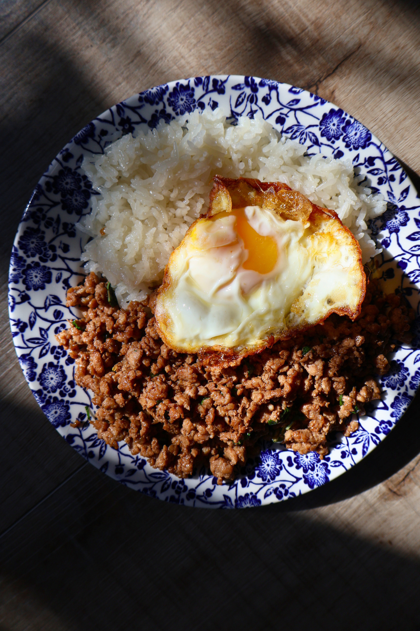 Thai pad kra pao with jasmine rice and crispy fried egg in natural shadow lighting