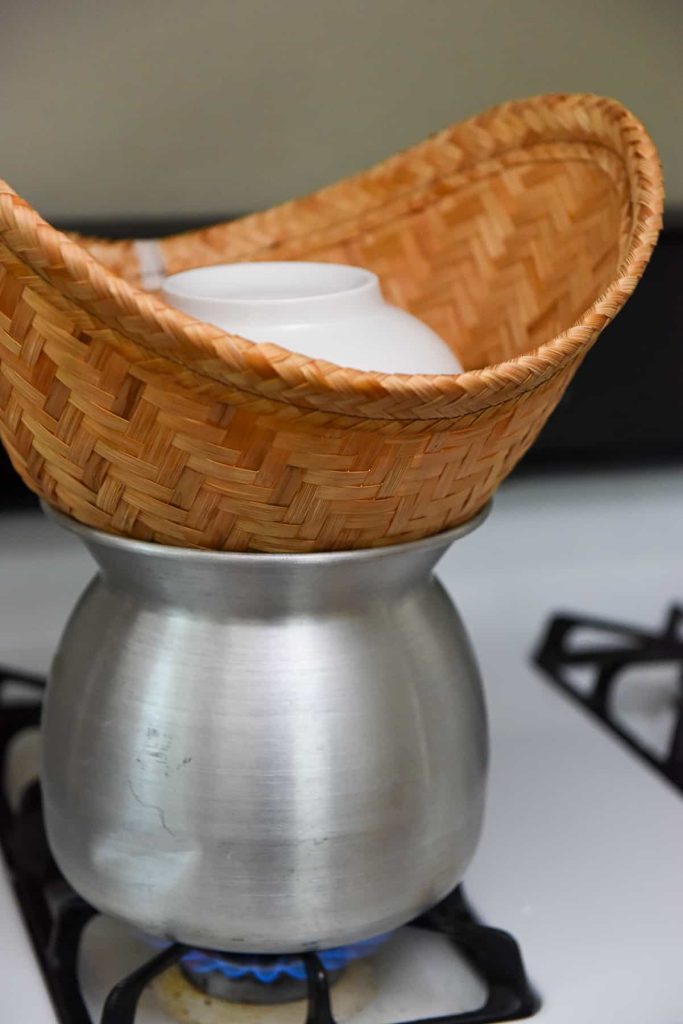 Traditional Thai bamboo sticky rice steamer basket on pot over stovetop