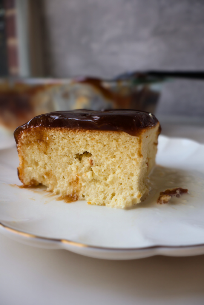 Slice of Balkan trilece cake soaked in milk and topped with glossy caramel on a white dessert plate