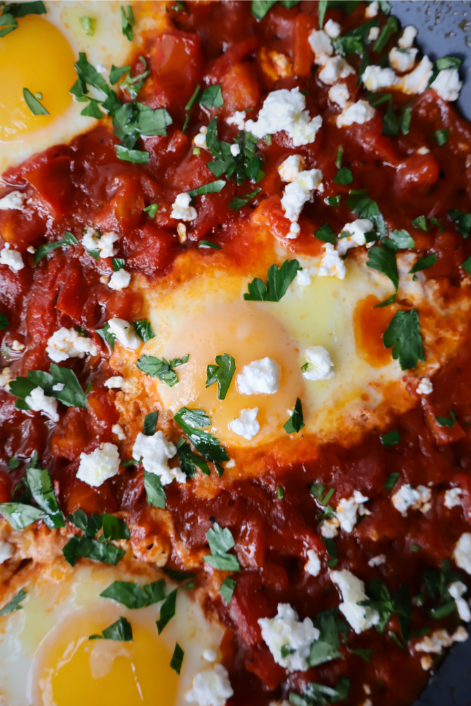 Extreme close up of shakshuka showing a runny egg yolk surrounded by rich red tomato sauce, Bulgarian feta crumbles, and fresh parsley