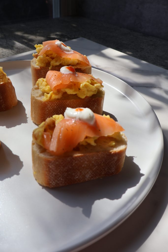 Angled view of smoked salmon and Boursin scrambled egg baguette bites on a white plate showing the layers of golden toasted baguette, creamy scrambled eggs, and folded smoked salmon