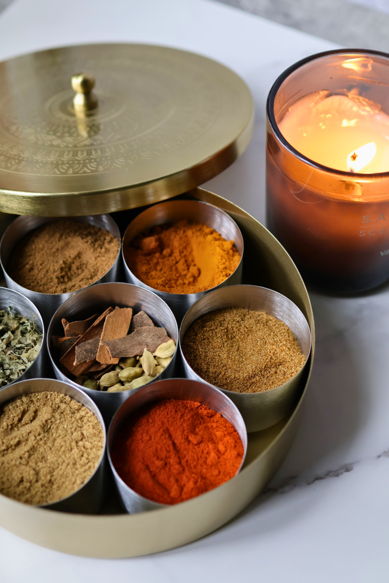 Gold masala dabba filled with Indian spices including turmeric, red chili powder, cinnamon, cardamom, and ground cumin