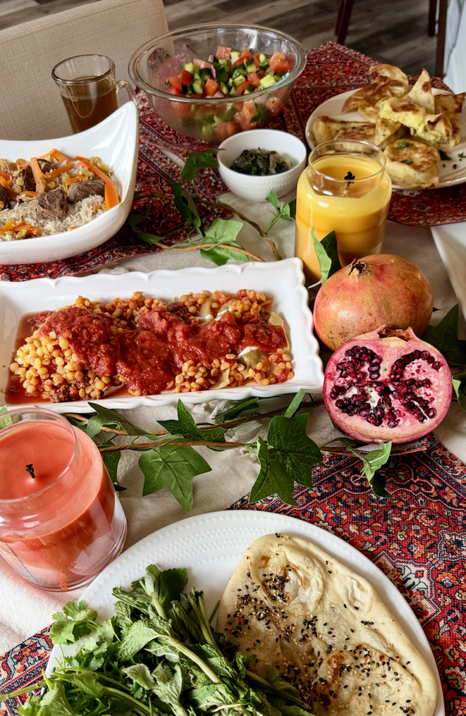 Afghan-inspired dinner table featuring mantu, borani banjan, Afghan salad, bolani, doogh, fresh naan, and pomegranates.
