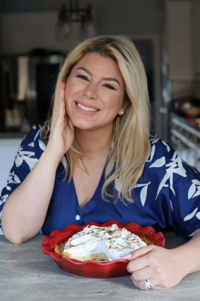 Food creator Emilia Kim smiling and holding a homemade key lime pie with toasted meringue in a red ceramic pie dish