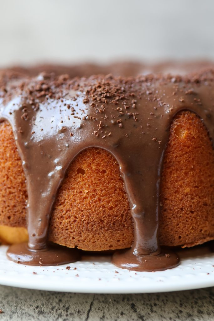 Whole Brazilian carrot cake (bolo de cenoura) bundt with chocolate glaze dripping down the sides on a white plate.