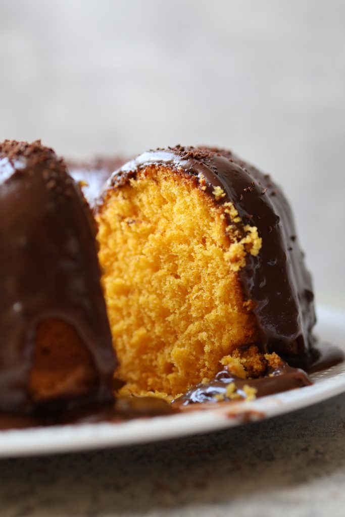 Slice of Brazilian carrot cake (bolo de cenoura) showing bright orange interior with chocolate glaze dripping down the side