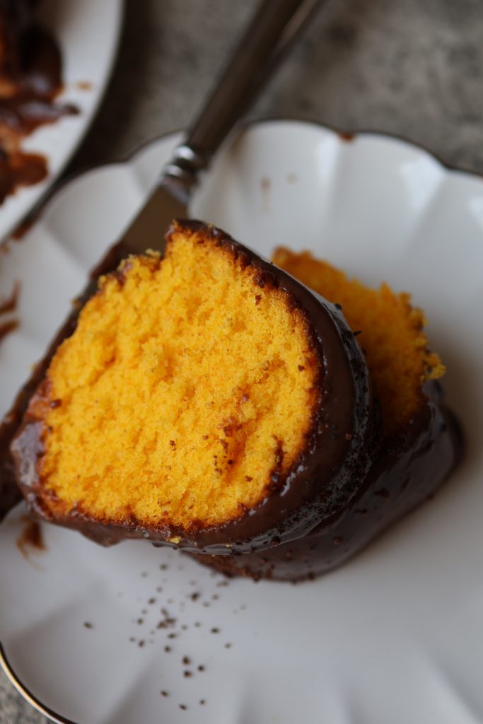 Overhead view of a slice of Brazilian carrot cake (bolo de cenoura) with chocolate glaze on a scalloped white plate with a fork