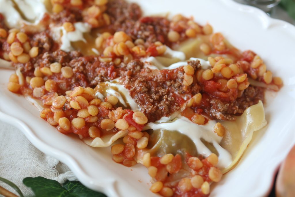 Traditional Afghan mantu dumplings topped with garlic yogurt, lentils, and seasoned meat sauce.