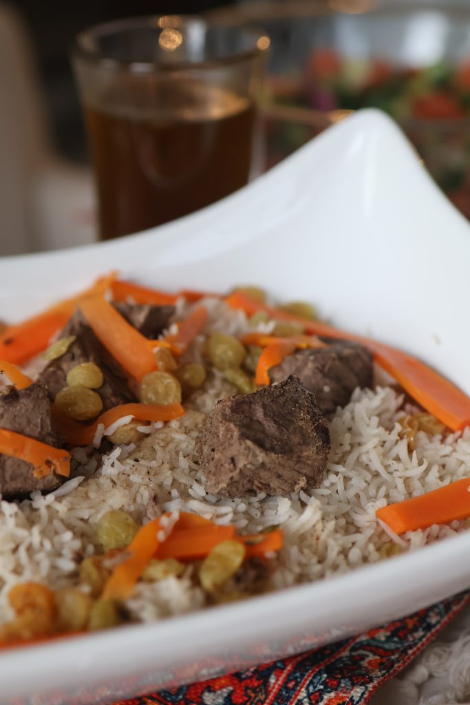 Traditional Afghan Kabuli Palau made with seasoned rice, beef, carrots, and raisins, served on a white platter.